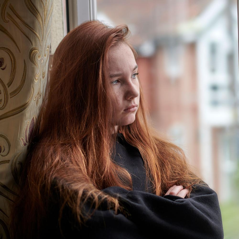 A girl unhappily looks out of a window