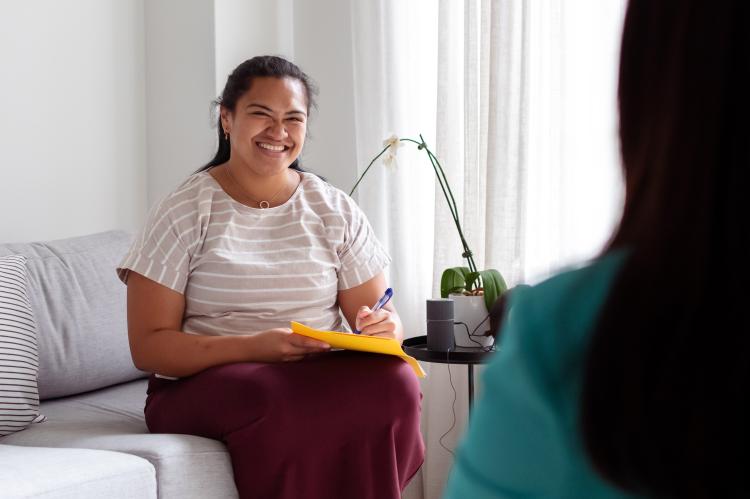 A social worker sits and smiles while holding a pad and pen