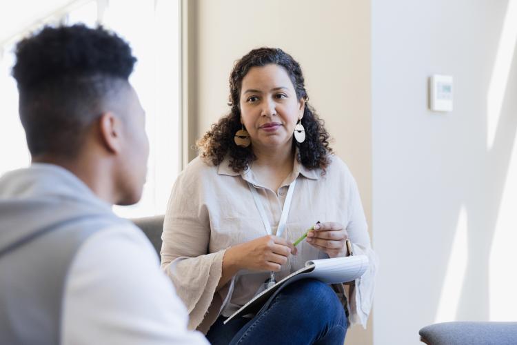 A woman holds a pen and listens to a boy providing feedback